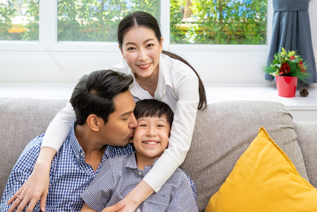 happy asian father, mother, and son sitting together on sofa in